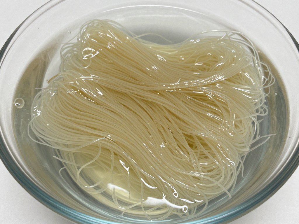 Longkou vermicelli being soaked in a bowl of warm water, showing the transformation from dry to pliable